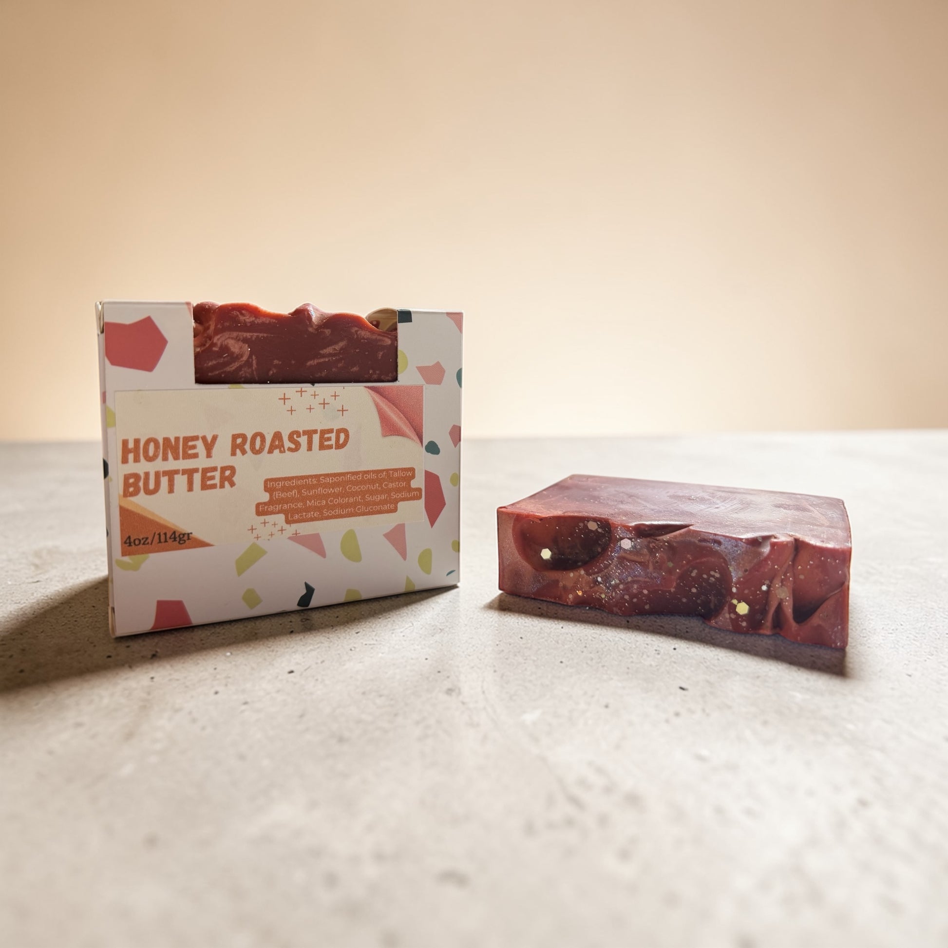 Bar of honey roasted butter soap next to its packaging on a light surface.