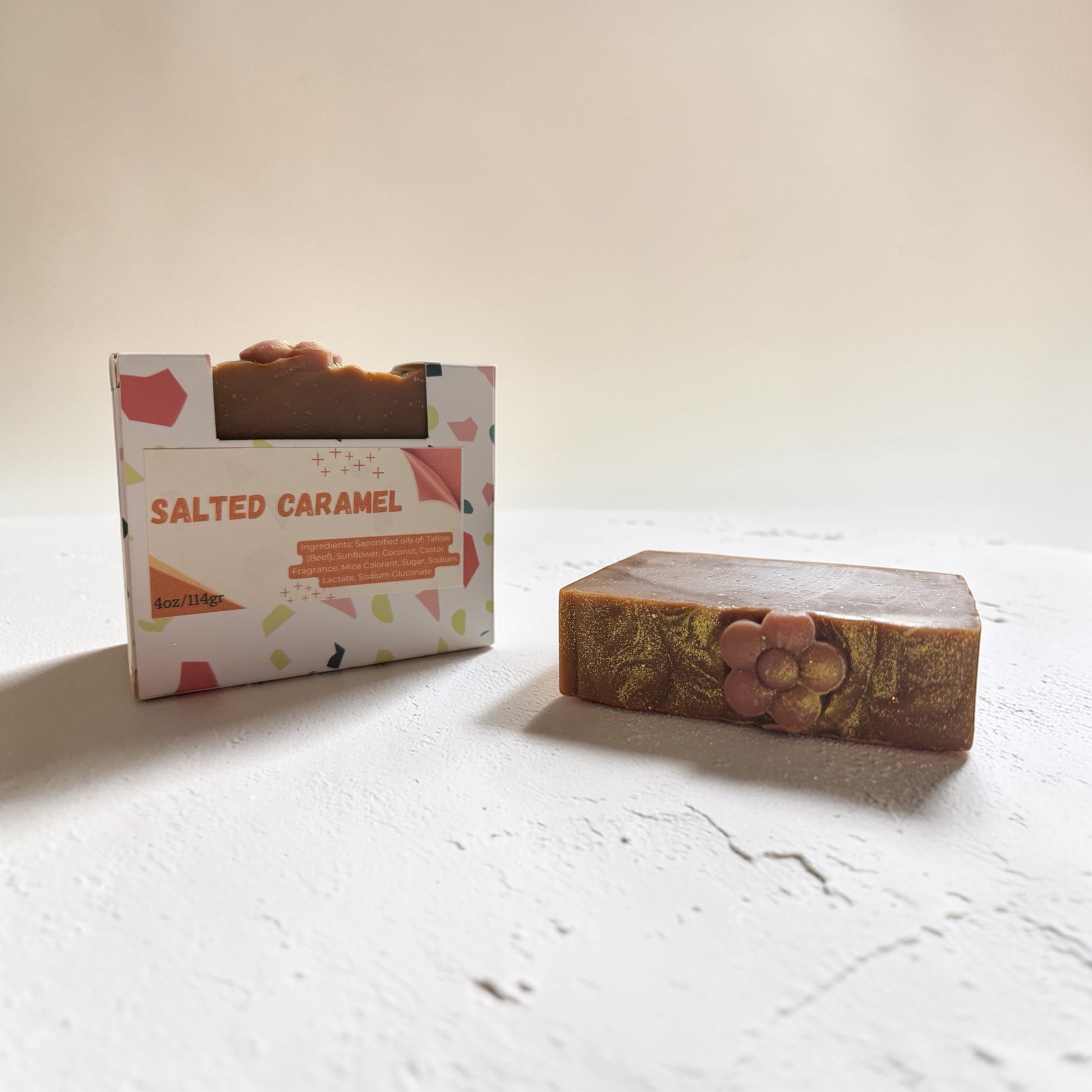 Bar of salted caramel soap next to its packaging on a light surface